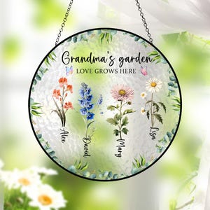 May include: A round, white, glass garden sign with the text "Grandma's garden LOVE GROWS HERE" and four floral designs with names "Alex", "David", "Mary", and "Lisa" written below each flower.