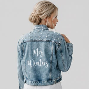 May include: A light blue denim jacket featuring white pearl embellishments across the upper back and shoulders. The back of the jacket displays the white text Mrs. Winters, while the collar features the date 04.10.24 in white lettering.