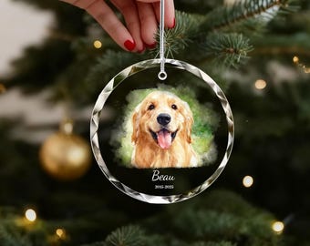 Könnte beinhalten: Ein klarer, runder Weihnachtsschmuck mit einem Aquarellgemälde eines Golden Retriever-Hundes. Der Name des Hundes, "Beau", und die Jahre "2015-2025" sind darunter aufgedruckt. Der Schmuck wird von einer Hand mit rotem Nagellack gehalten.