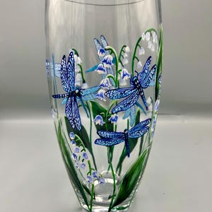 May include: A clear glass vase with a hand-painted design of blue dragonflies and white lily of the valley flowers.