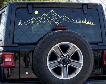 May include: Black Jeep Wrangler with a yellow mountain range and trees decal on the rear window. The Jeep has a spare tire on the back.