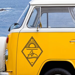 Peut inclure: Un van jaune vif arborant un autocollant noir en forme de losange sur le panneau latéral. L'autocollant présente une illustration au trait d'une personne sur un jet ski au-dessus de vagues sous un soleil levant, le tout dans un cadre géométrique.