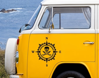 May include: A bright yellow van featuring a black vinyl decal on the side panel. The decal displays a compass rose design with a skull and crossbones at the center, surrounded by the cardinal direction letters N, S, E, and W in a bold font.