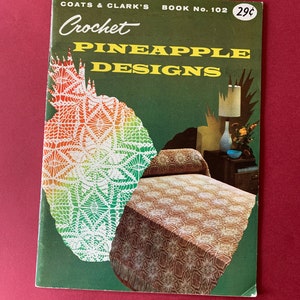 May include: A vintage crochet pattern book with a green cover and the title "Coats & Clark's Crochet Pineapple Designs" in yellow lettering. The book cover features a close-up of a crocheted pineapple design and a bedspread with a pineapple pattern.