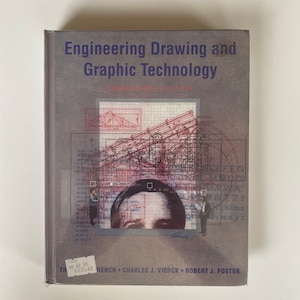 May include: A grey hardback textbook titled "Engineering Drawing and Graphic Technology" with a geometric design on the cover. The cover features a red and black design with a person in a suit standing in the middle of the design. The book is priced at £135.40.