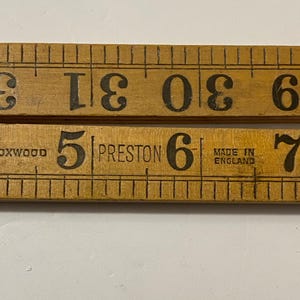 May include: Close-up of two antique wooden folding rulers. The top ruler displays measurements from 28 to 33 inches, while the bottom ruler shows measurements from 4 to 8 inches. The bottom ruler is marked "BOXWOOD" and "PRESTON", with "MADE IN ENGLAND".