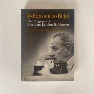Peut inclure: Une photo en noir et blanc du président Lyndon B. Johnson sur la couverture d'un livre intitulé "To Heal and to Build: The Programs of President Lyndon B. Johnson". Le livre est édité par James MacGregor Burns.
