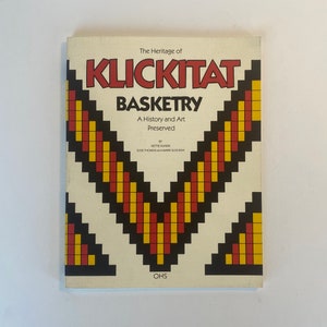 May include: A book titled "The Heritage of Klickitat Basketry: A History and Art Preserved" by Nettie Kunex, Elsie Thomas, and Marie Slockish. The cover features a geometric design in red, yellow, and black.