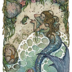 May include: A watercolour illustration titled The Seashore by Tavera Grace featuring a mermaid with long brown hair resting on a sandy beach with sea foam, green seaweed, grey rocks, starfish, and a small crab. The artwork has a soft colour palette.
