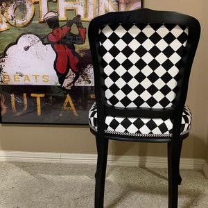 May include: Black and white checkered dining chair with a black wooden frame. The chair has a curved back and a padded seat.