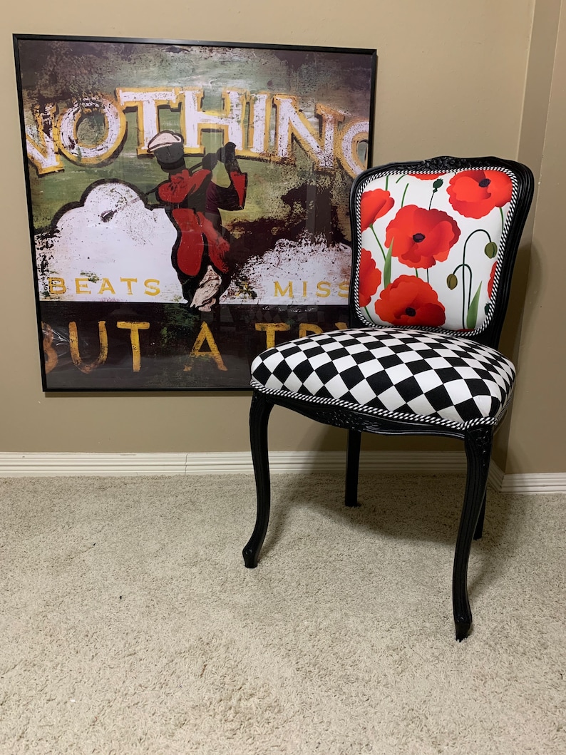 May include: A black and white checkered chair with a black frame and a red poppy floral patterned back cushion. The chair is sitting on a beige carpet in front of a framed print with the text "Nothing Beats But A Try" and a golfer in the image.