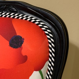 May include: Close-up of a black chair with a white and black striped trim. The chair is upholstered in a white fabric with a red poppy print.