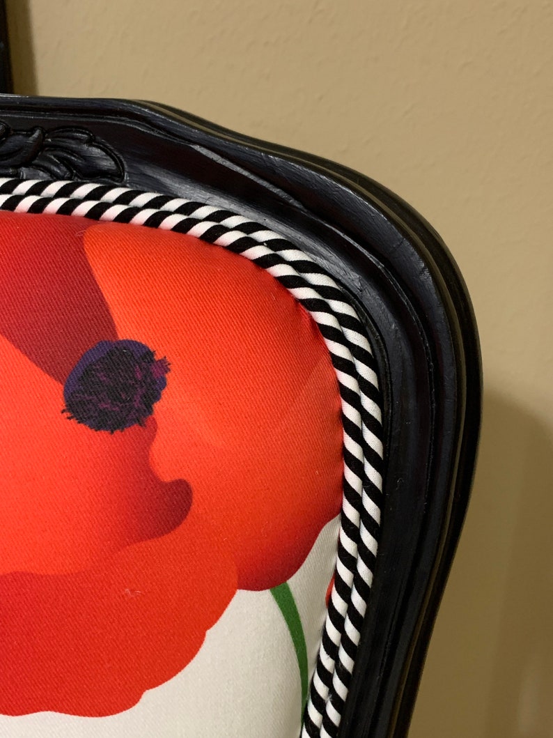 May include: Close-up of a black chair with a white and black striped trim. The chair is upholstered in a white fabric with a red poppy print.