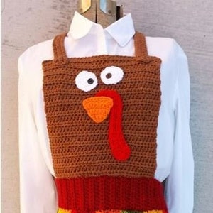 May include: A crocheted turkey-themed apron with a brown turkey face and a colorful striped skirt. The apron is made with brown, red, orange, yellow, and green yarn.