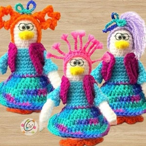 May include: Three crocheted stuffed toys shaped like birds with colorful yarn accents. The birds are wearing dresses and have glasses. The birds are standing on a wooden surface.