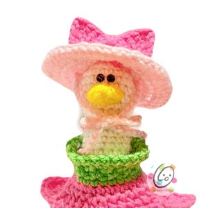 May include: A crocheted doll wearing a pink hat with a bow, a green and pink dress, and a colorful flower-shaped base.