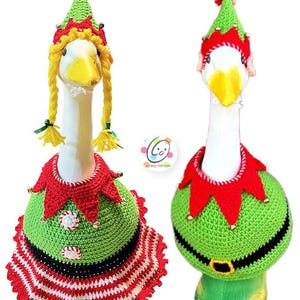 May include: Two white geese wearing green and red elf costumes with pointy hats. The costumes are crocheted and feature a red and white striped skirt, a green vest, a red collar, and a black belt. The geese are facing forward with their heads tilted slightly to the side.