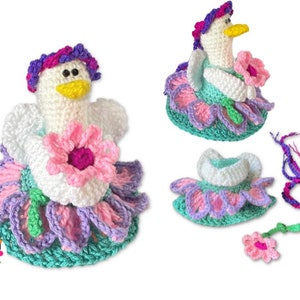 May include: A crocheted chicken doll wearing a pink, purple, and green flower-shaped dress. The chicken has a white body, yellow beak, and pink and purple yarn for hair. The doll is holding a pink flower.