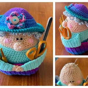 May include: A crocheted granny doll with a purple and blue hat, holding a pair of scissors and crochet hooks. The doll is a handmade craft item.