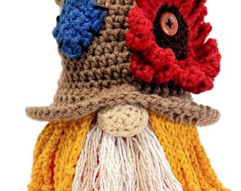 May include: A crocheted gnome with a brown hat, a red flower, and a yellow beard. The gnome is wearing a blue and white eye patch. A small black bird sits on top of the hat.