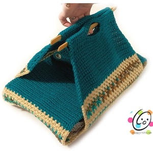 Puede incluir: Bolso de mano de crochet de color turquesa con ribete marrón y beige. El bolso tiene dos asas de madera y un cierre de presión.