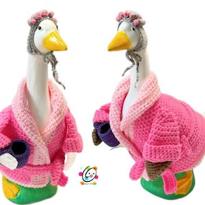 May include: Two white ceramic geese wearing pink crocheted robes and grey crocheted hats with pink flowers. The geese are holding purple crocheted mugs.