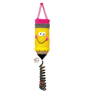 May include: A crochet hanging bag shaped like a yellow pencil with a pink eraser top, a grey band, and a black pointed tip. The pencil features a white face with two round eyes and a black stitched smile, with pink cheeks and a hanging strap.