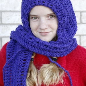 May include: A person wearing a handmade, royal blue crochet hood and scarf set. The hood covers the head and neck, and the scarf drapes over a red jumper. The crochet work has a textured appearance.