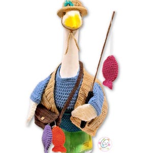 May include: A whimsical, handmade goose figurine dressed as a fisherman. The goose wears a straw hat, a blue sweater, and a tan vest. It carries a fishing rod with a pink fish and a brown satchel with colorful fish charms. The figurine is set against a white background.