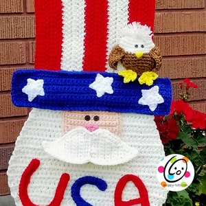 May include: Crocheted patriotic Uncle Sam door hanger with red, white, and blue stripes, a blue hat with white stars, a white beard, and the word "USA" in red and blue. A crocheted bald eagle sits on top of the hat.