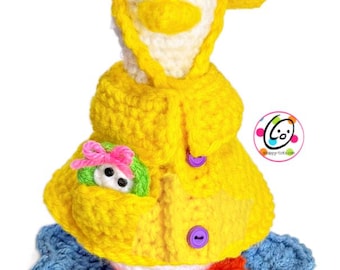 May include: A handmade crochet duckling wearing a yellow coat and hat, with a small toy in its pocket. The duckling has a white face, orange feet, and is sitting on a blue crocheted base. The coat has purple buttons.