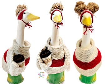 May include: Three ceramic goose figurines wearing crocheted hats and sweaters. The geese are wearing red and white sweaters and hats with brown yarn accents.