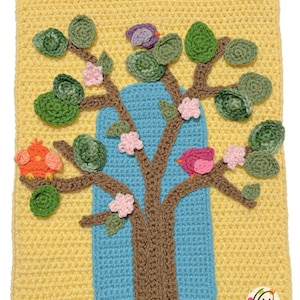 Può includere: Un arazzo da parete all'uncinetto con un albero marrone con un tronco blu, foglie verdi, fiori rosa e tre uccelli colorati. Lo sfondo è giallo.