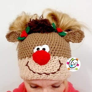 May include: A brown crocheted reindeer hat with a red pom-pom nose, green holly leaves, and white eyes. The hat has two brown crocheted antlers and brown yarn hair.