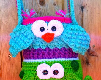 May include: A crocheted owl and frog bag with a pink, blue, purple, green, and white color scheme. The bag has a long strap and is perfect for carrying small items.