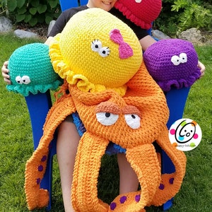 May include: A crocheted octopus plush toy with purple and orange tentacles. The octopus is sitting on a blue chair with a child holding it. There are three crocheted jellyfish plush toys in the background, one red, one yellow, and one green.