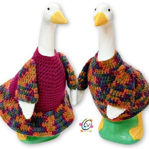 May include: Two ceramic geese wearing crocheted sweaters. One goose is wearing a burgundy sweater with a multi-colored pattern, and the other goose is wearing a multi-colored sweater with a blue, green, and orange pattern.