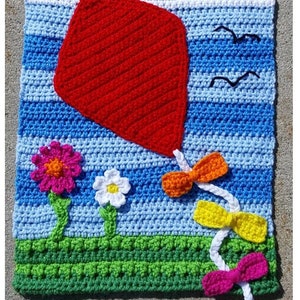 May include: A crocheted wall hanging featuring a red kite flying in a blue sky with white clouds. The sky is bordered by a yellow sun with white rays and a green grassy field. The kite has a white string with three colorful bows.
