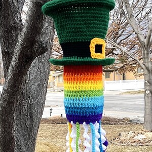 May include: A crocheted rainbow wind chime with a green leprechaun hat at the top. The hat has a black band and a gold buckle. The rainbow is made of different colored yarn and the bottom of the chime has white crocheted shamrocks.