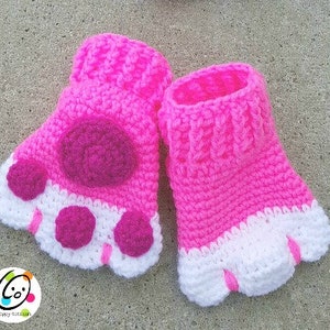 May include: A pair of pink and white crocheted paw-shaped fingerless gloves. The gloves have a pink paw print on the back and white toes.