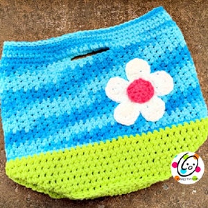 May include: A crocheted tote bag with a blue and green color scheme. The bag has a white flower with a pink center on the front. The bag has a handle and is made with a soft yarn.