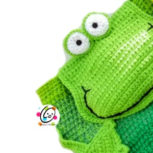 May include: Green crocheted frog blanket with white eyes and a black mouth. The blanket is made with a gradient of green yarn, starting with a darker green at the bottom and fading to a lighter green at the top.