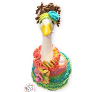 May include: A white goose wearing a colorful crocheted dress with a flower accent and a brown crocheted hat with a blue flower accent.