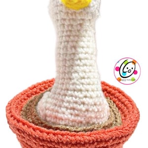 May include: A handmade crochet goose toy with a white body, a yellow beak, and black eyes. The goose is set in a crochet basket with orange, brown, and beige layers. The toy is likely for children.