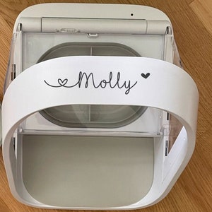 Könnte beinhalten: Weißer Plastik-Tierfutterspender mit einem durchsichtigen Plastikdeckel und einer grauen herausnehmbaren Schüssel. Der Spender hat ein Etikett mit der Aufschrift "Molly" und einem Herz auf jeder Seite.