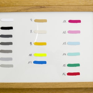 May include: A framed color palette featuring 18 paint swatches in various shades. The swatches are numbered and include colors like white, black, gray, yellow, blue, pink, and green. The frame is made of light-colored wood.