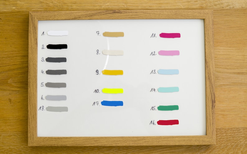 May include: A framed color palette featuring 18 paint swatches in various shades. The swatches are numbered and include colors like white, black, gray, yellow, blue, pink, and green. The frame is made of light-colored wood.