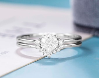 May include: A silver engagement ring with a round centre stone and a halo of smaller stones. The ring is set on a white background.