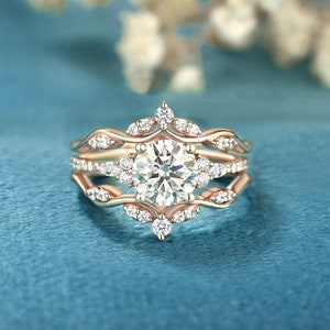 May include: A rose gold engagement ring set with a large round centre stone and smaller accent stones. The ring has a delicate, floral design.