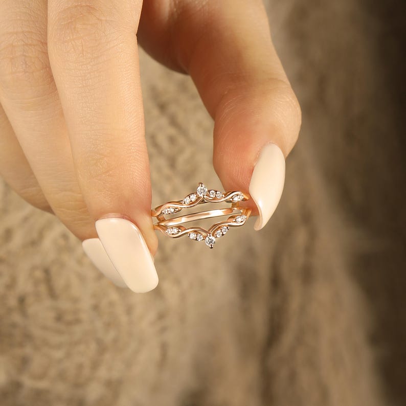 Pu&ograve; includere: Un delicato anello in oro rosa con piccoli diamanti scintillanti. L'anello presenta un design unico con due bande intrecciate e accentuate da una fila di diamanti.